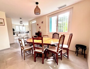 Un coin repas avec une grande table en bois et six chaises, un luminaire suspendu et une fenêtre donnant sur un paysage verdoyant.