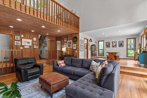 A spacious living room with a grey sectional sofa, a leather armchair, and a wooden staircase. - Cozy modern style home 4.4 miles from Augusta National (Augusta)