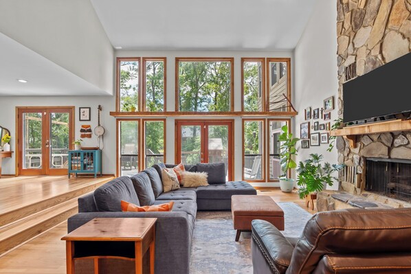 A spacious living room with a large sectional sofa, a fireplace, and large windows offering a view of the outdoors. - Cozy modern style home 4.4 miles from Augusta National (Augusta)