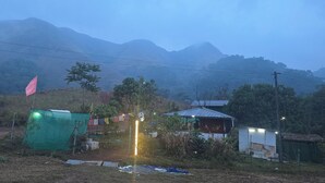 A rural setting with a dirt path, a green structure, a small white building, and a flag. - NOMADIC MOUNTY SATHRAM  (Peermade)