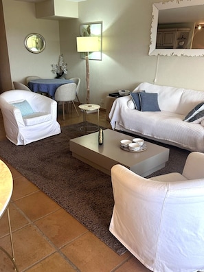 Ein Wohnzimmer mit einer Couch, zwei Sesseln, einem Couchtisch und einem Essbereich mit Tisch und Stühlen.