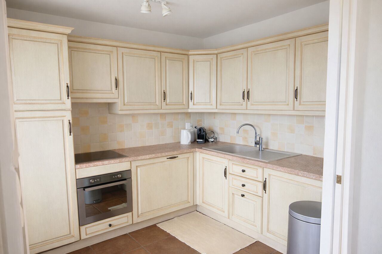 A kitchen with light-colored cabinets, a stainless steel sink, a built-in oven, and a tiled backsplash.