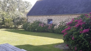 A stone building with a small window, surrounded by a well-maintained lawn and flowering bushes. - Chic and authentic bourgeois house by the sea, ideal for surfing, beaches and hiking. (Tréguennec)