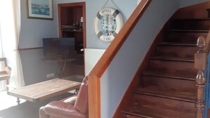 A staircase with wooden steps and a handrail, a leather sofa, a framed picture on the wall, and a small shelf with decorative items. - Chic and authentic bourgeois house by the sea, ideal for surfing, beaches and hiking. (Tréguennec)