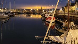 A marina at dusk with calm waters reflecting the lights. Boats are docked, and the marina is illuminated by ambient lighting. - Chic and authentic bourgeois house by the sea, ideal for surfing, beaches and hiking. (Tréguennec)