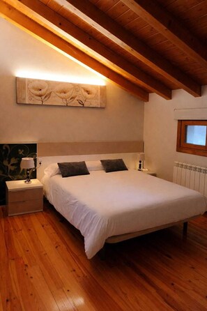 Une chambre avec un plafond en bois, un lit avec une literie blanche, une table de chevet avec une lampe et un radiateur.