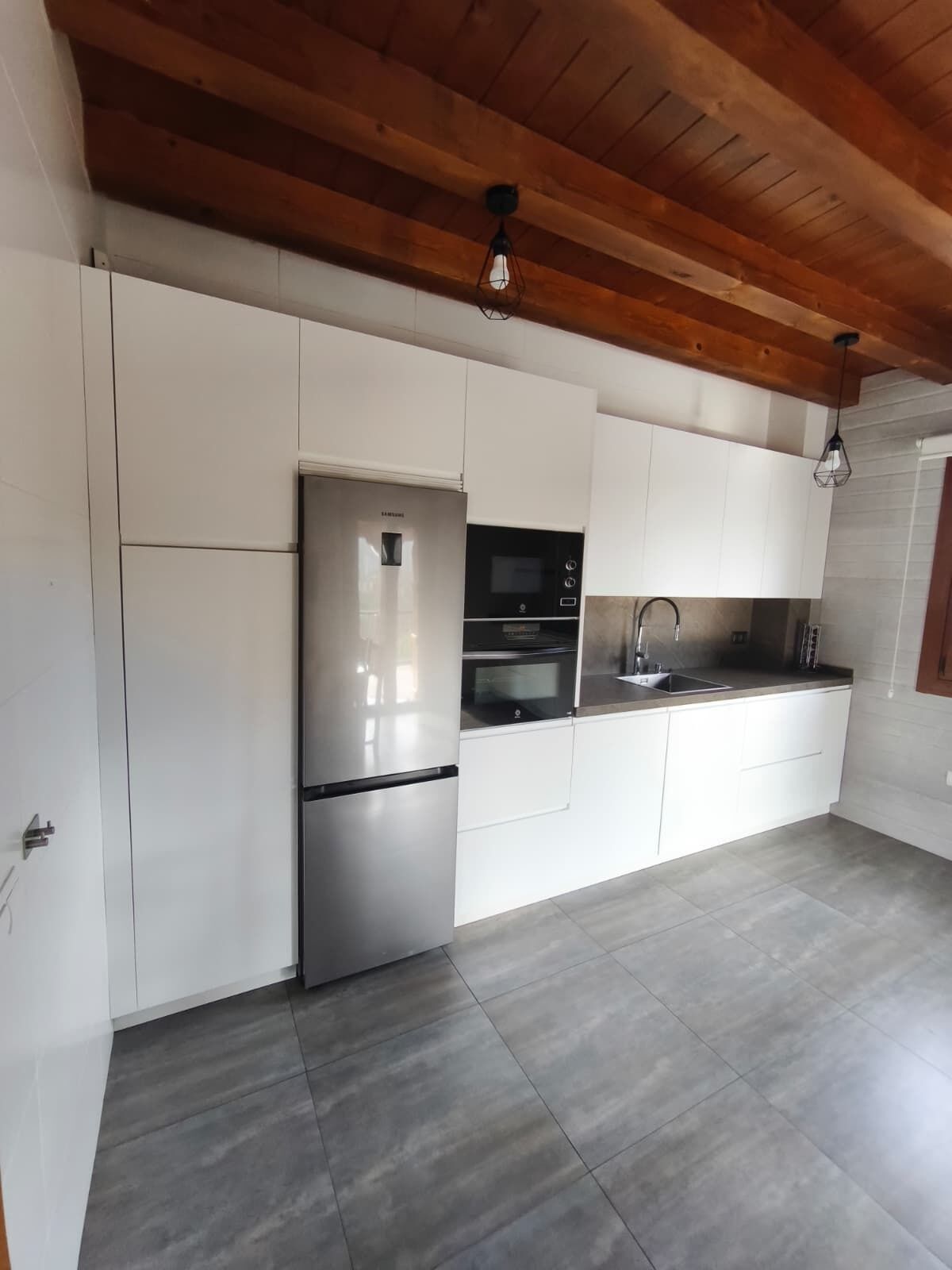 Una cocina moderna con armarios blancos, electrodomésticos de acero inoxidable y techo de madera.