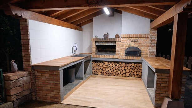 Een rustieke buitenkeuken met een bakstenen open haard, een spoelbak en een houten werkblad.