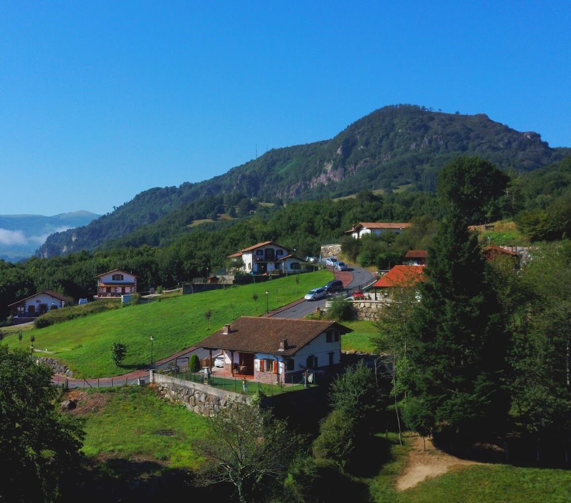 Un village rural avec des maisons construites sur une colline, entouré de verdure et avec une montagne en arrière-plan.