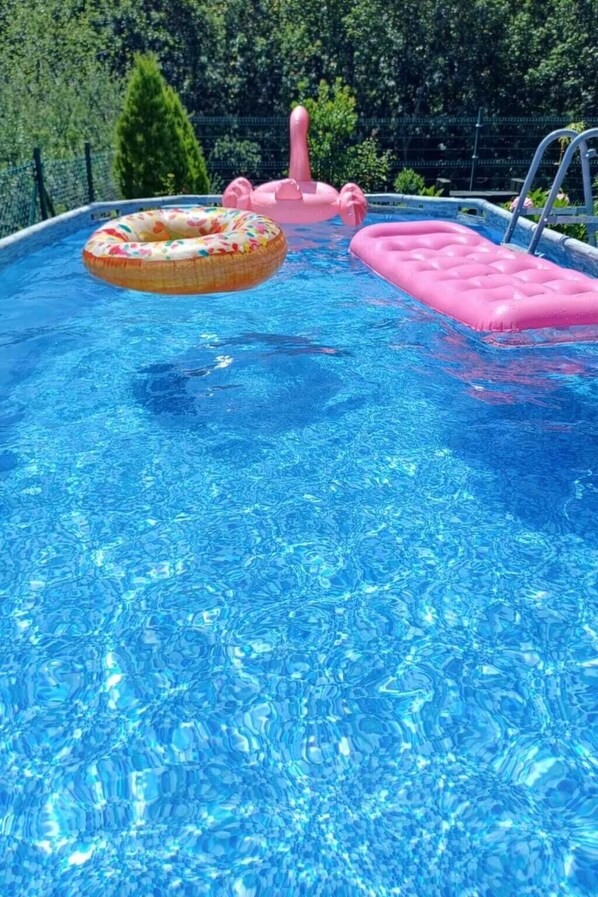 Une piscine avec une eau d’un bleu cristallin, un flotteur gonflable rose et un anneau gonflable à motifs floraux.