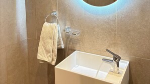Une salle de bain moderne avec un lavabo blanc, un miroir rond avec un éclairage intégré et un porte-serviettes.