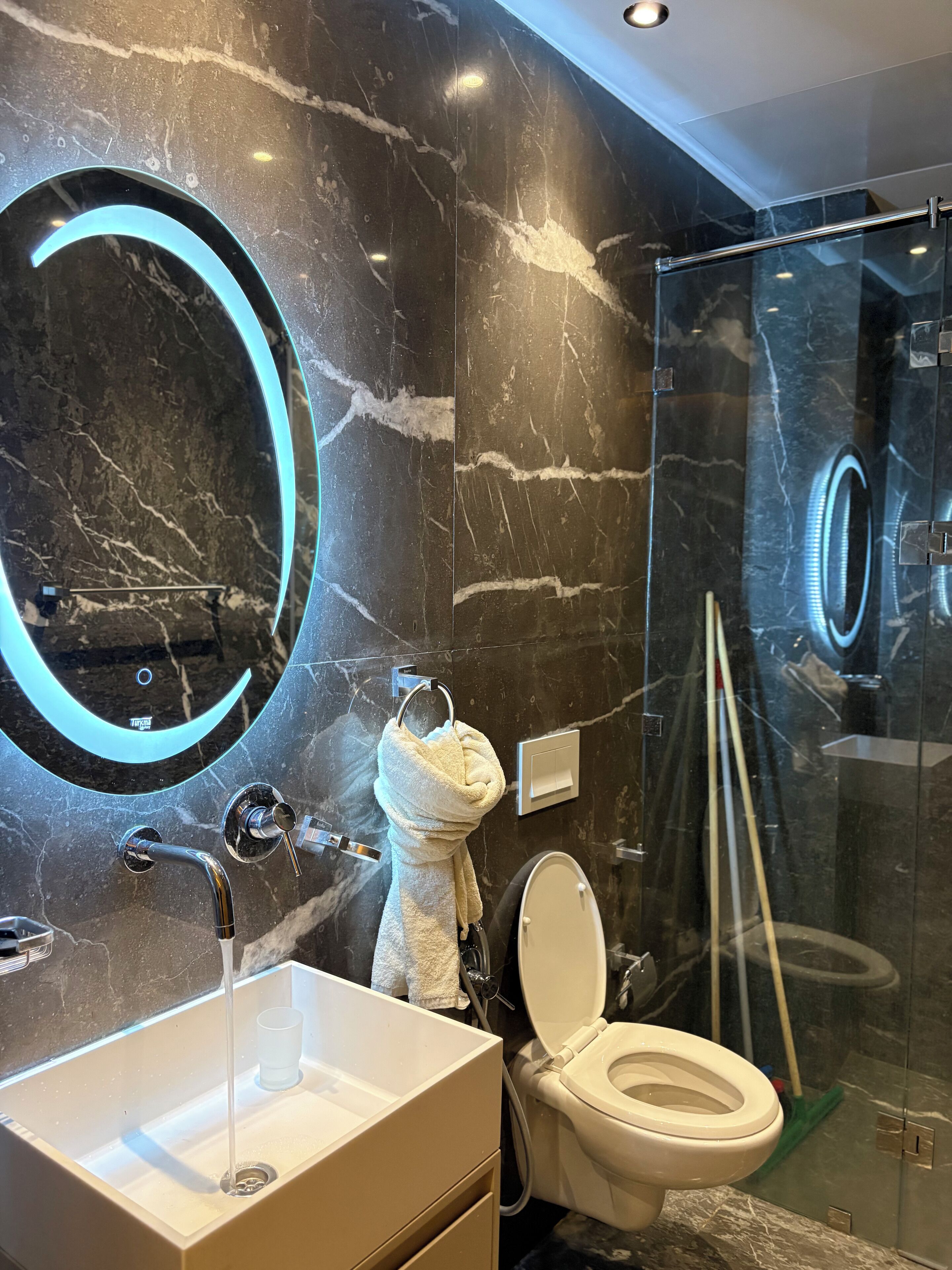 Un bagno moderno con lavabo in marmo, uno specchio rotondo illuminato e cabina doccia in vetro.