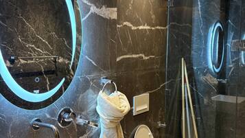 Un bagno moderno con lavabo in marmo, uno specchio rotondo illuminato e cabina doccia in vetro.