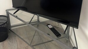 Un televisor de pantalla plana sobre un soporte de vidrio en una habitación con piso de madera.