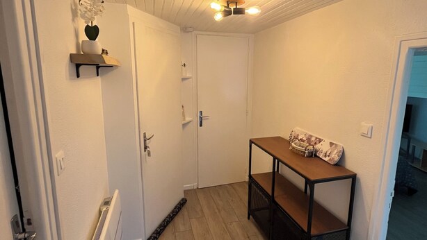 Un pasillo con piso de madera, un radiador blanco, una puerta y una mesa con un monopatín.