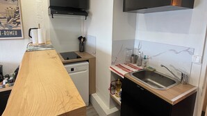 Una cocina compacta con encimera de madera, lavavajillas integrado, campana extractora negra y un lavamanos de acero inoxidable.