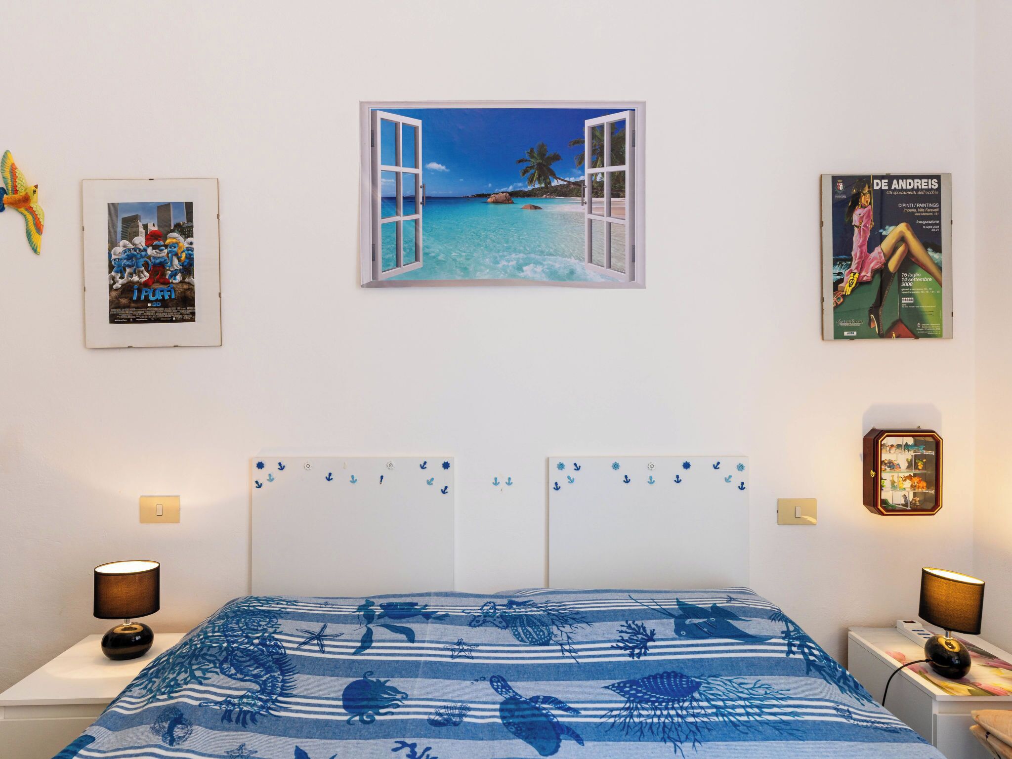 A bedroom with a bed, a poster of a beach scene, a poster of a movie, and a poster of a painting.