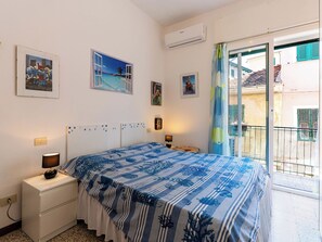 Quarto com cama, mesa de cabeceira, ar condicionado fixado na parede e janela com vista para um edifício.