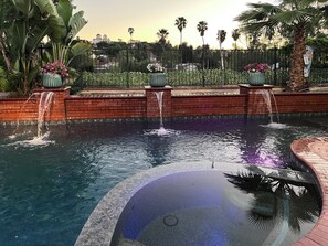 Ein Pool mit Wasserspielen, umgeben von Ziegelmauern und Kübelpflanzen.