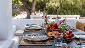 Una mesa al aire libre preparada para dos personas, con platos, vasos y una cesta de frutas.