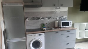 Een compacte keuken met een wasmachine, magnetron en een inbouwoven.