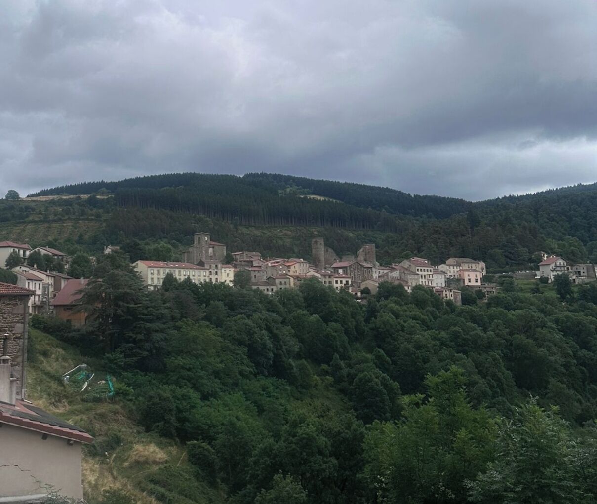 A historic town with medieval architecture, surrounded by dense forests and hills.