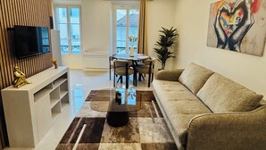 A modern living room with a sofa, a coffee table, a TV, and a dining area. - Luxury design apartment Cannes Centre - 2 mn Palais du Festival and Croisette (Cannes)