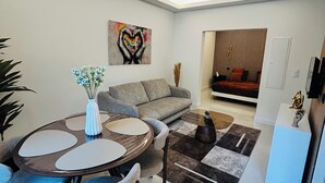 A modern living room with a round dining table, grey sofa, and a painting of hands forming a heart. - Luxury design apartment Cannes Centre - 2 mn Palais du Festival and Croisette (Cannes)