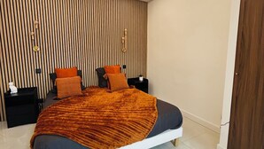 A modern bedroom with a large bed, a nightstand, a wall-mounted lamp, and a wooden panel wall. - Luxury design apartment Cannes Centre - 2 mn Palais du Festival and Croisette (Cannes)