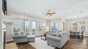 A spacious living room with a gray sofa set, a wooden coffee table, and a dining area with a table and chairs. - Beach and Bay views | Family & pet friendly | Golf cart (Galveston)