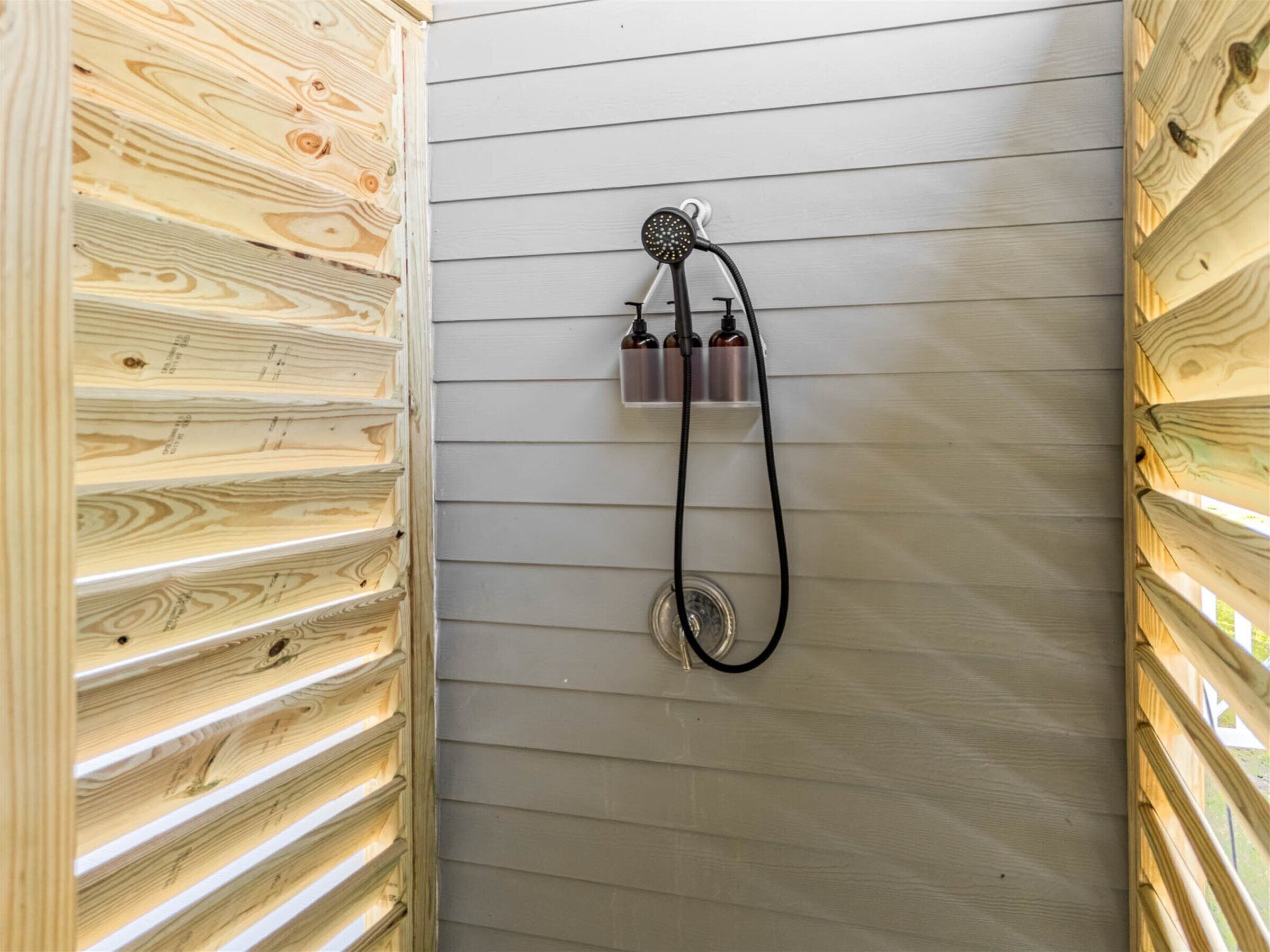 A shower with a wooden panel wall, a handheld showerhead, and three bottles of shampoo.