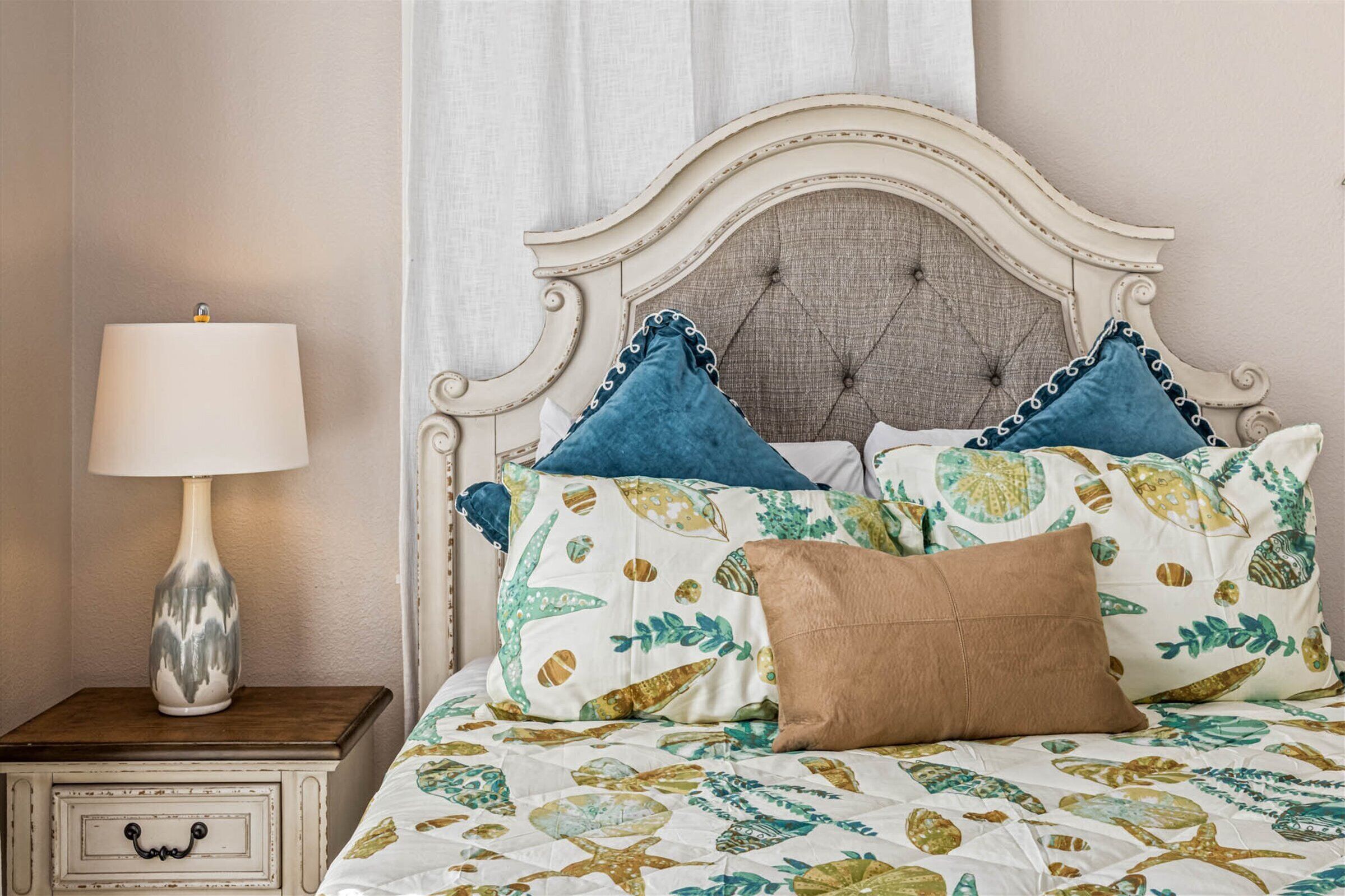 Een slaapkamer met een bed, kussens, een nachtkastje en een lamp.