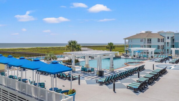 A resort pool area with lounge chairs and umbrellas, a large pool, and a view of the ocean. - Beach and Bay views | Family & pet friendly | Golf cart (Galveston)