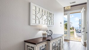 A hallway with a wooden cabinet, a decorative wall piece, and a door leading to an outdoor area. - Beach and Bay views | Family & pet friendly | Golf cart (Galveston)