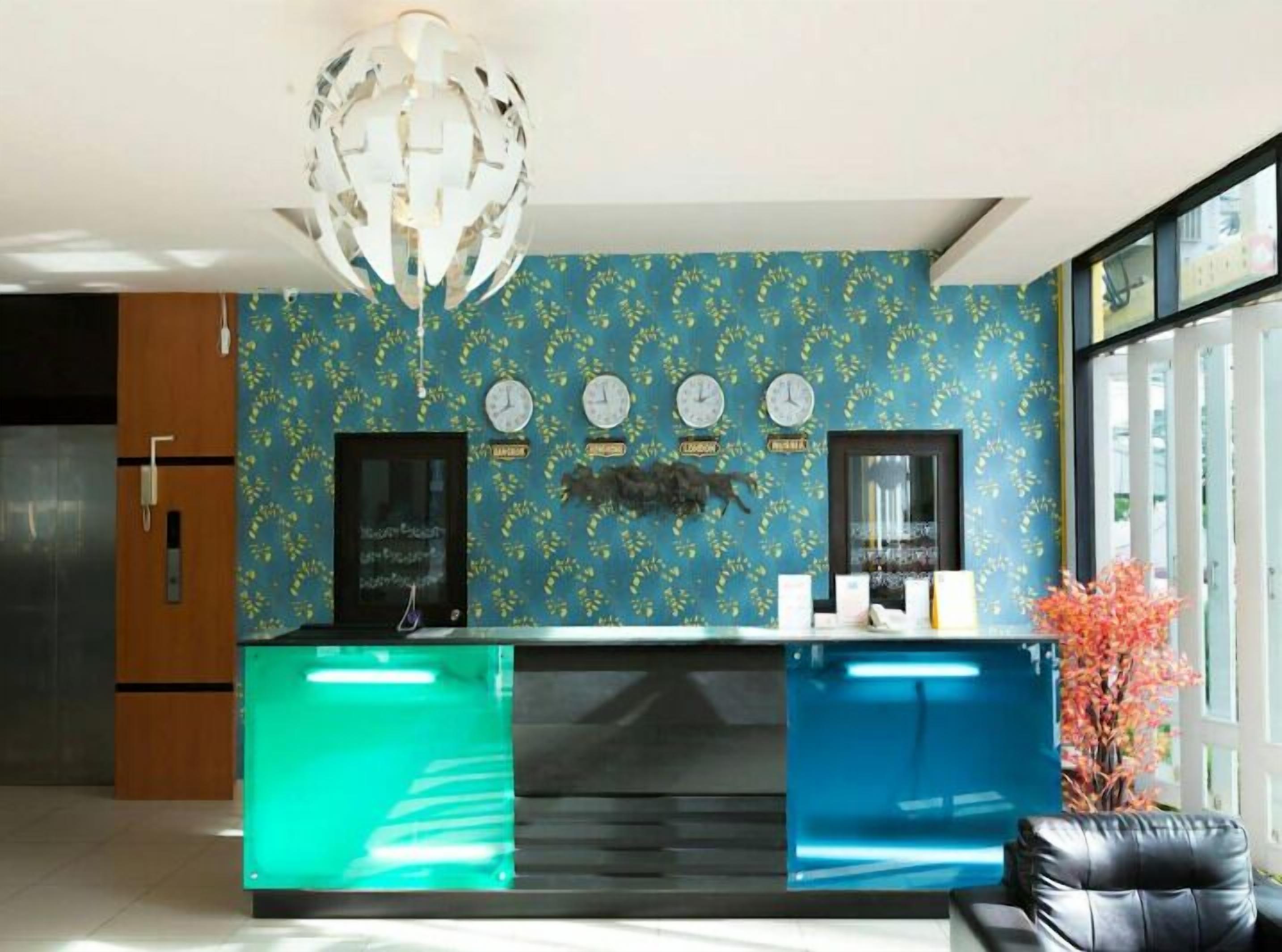A reception desk with a blue and green color scheme, a chandelier, clocks, and a plant.
