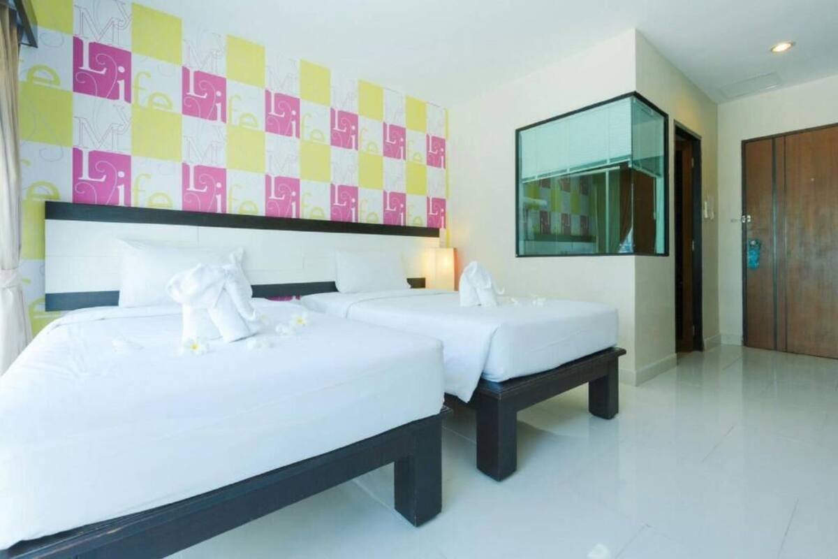 A hotel room with two beds, a large mirror, and a colorful wall design.