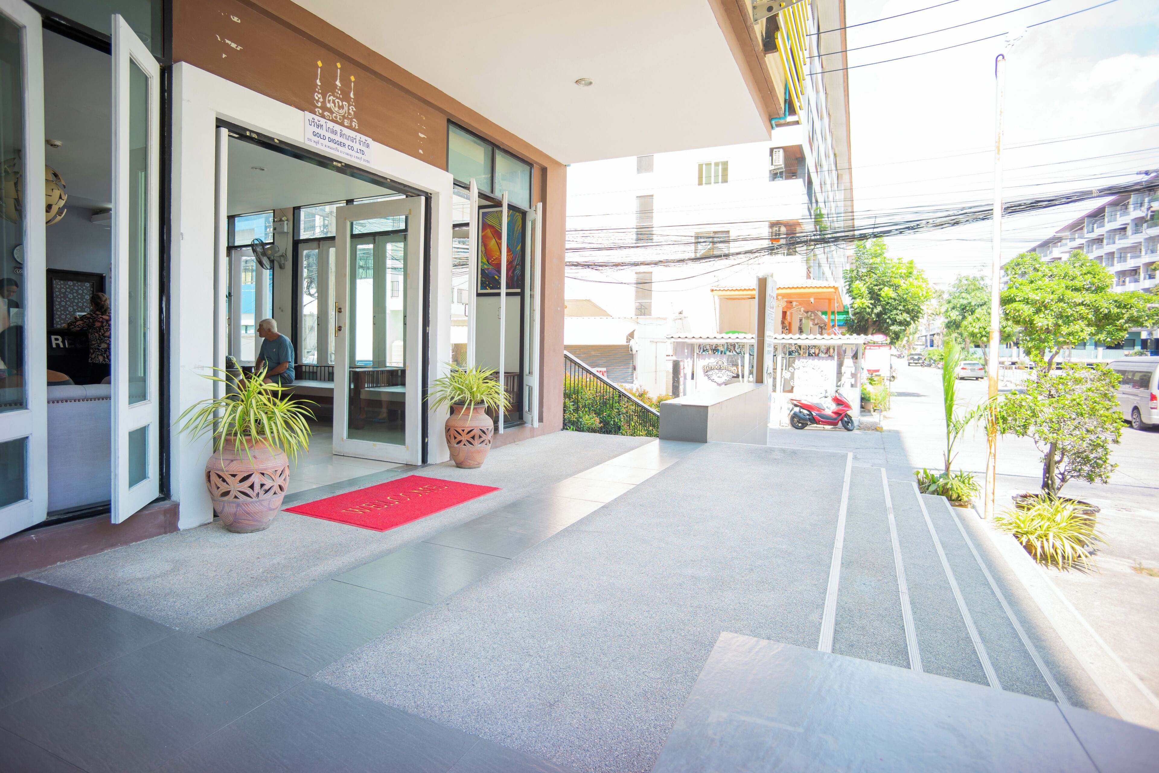 Entrada de un hotel con alfombra roja, plantas en macetas y una escalera que lleva a la entrada.