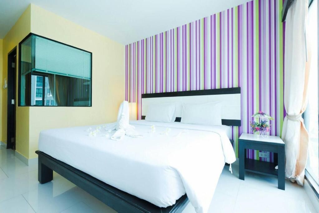 A modern hotel room with a large bed, a bedside table, a mirror, and a striped wall.