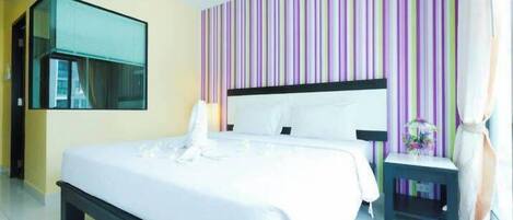 A hotel room with a bed, a bedside table, a mirror, and a striped wall.