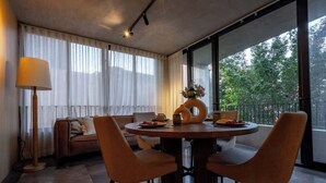Een moderne eetruimte met een ronde tafel, vier stoelen en een vaas met bloemen. Achtergrond is een bank en een vloerlamp.