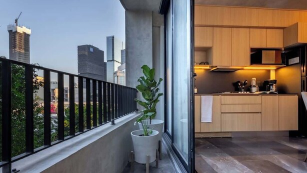 Een moderne keuken met houten kastjes en een zwart aanrecht, een potplant en een stadszicht door grote ramen.
