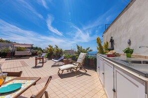 Eine Dachterrasse mit Essbereich, Liegestühlen und einer Küchenzeile.