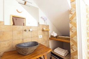 Ein Badezimmer mit einem Steingefäß, einem Holzkosmetikschrank, einem Handtuchhalter und einem Spiegel.