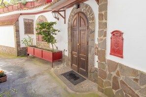 Ein Steinhaus mit einer großen Holztür, einem roten Briefkasten und einem Blumenkasten mit Grünpflanzen.
