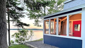 A house with a red door, large windows, and a view of a lake.
