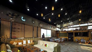 A spacious indoor area with a high ceiling, multiple seating arrangements, and a large window providing a view. - AARYA HOTEL & SPA Jim Corbett (Ramnagar)