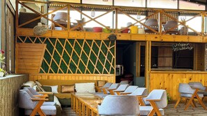 A cozy outdoor seating area with wooden furniture and a green lattice wall. - AARYA HOTEL & SPA Jim Corbett (Ramnagar)