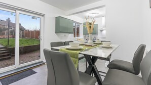 Ein moderner Essbereich mit einem Glastisch, grauen Stühlen und Blick in den Garten durch große Schiebetüren.