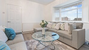 Ein Wohnzimmer mit Glastisch, beiger Couch und einer weißen Tür.