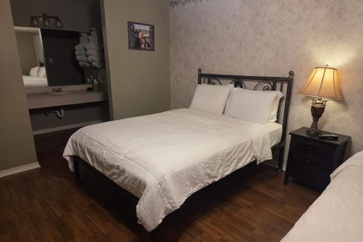 A bedroom with a bed, a nightstand with a lamp, a dresser, and a mirror.